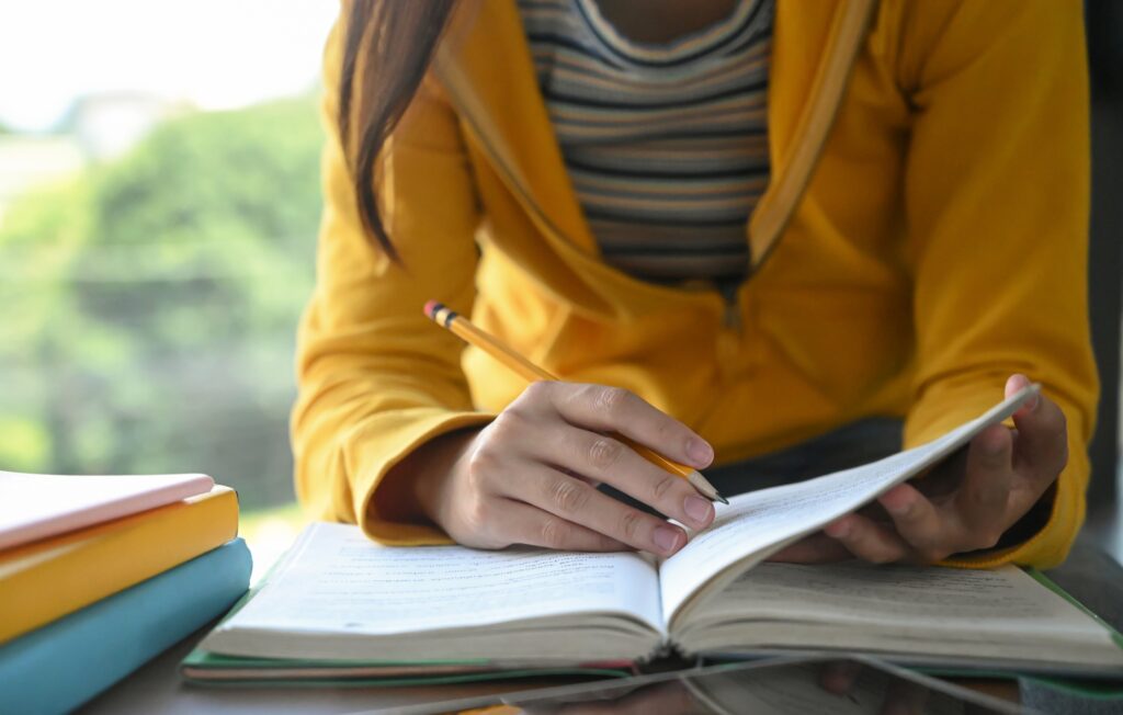 Students are reading books and taking notes for exam preparation.